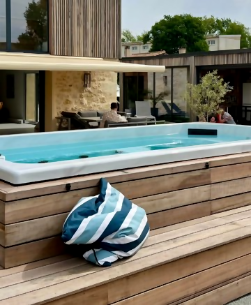 Jacuzzi sous pergola en bois avec piscine, arbres, buissons et maisons en arrière-plan.